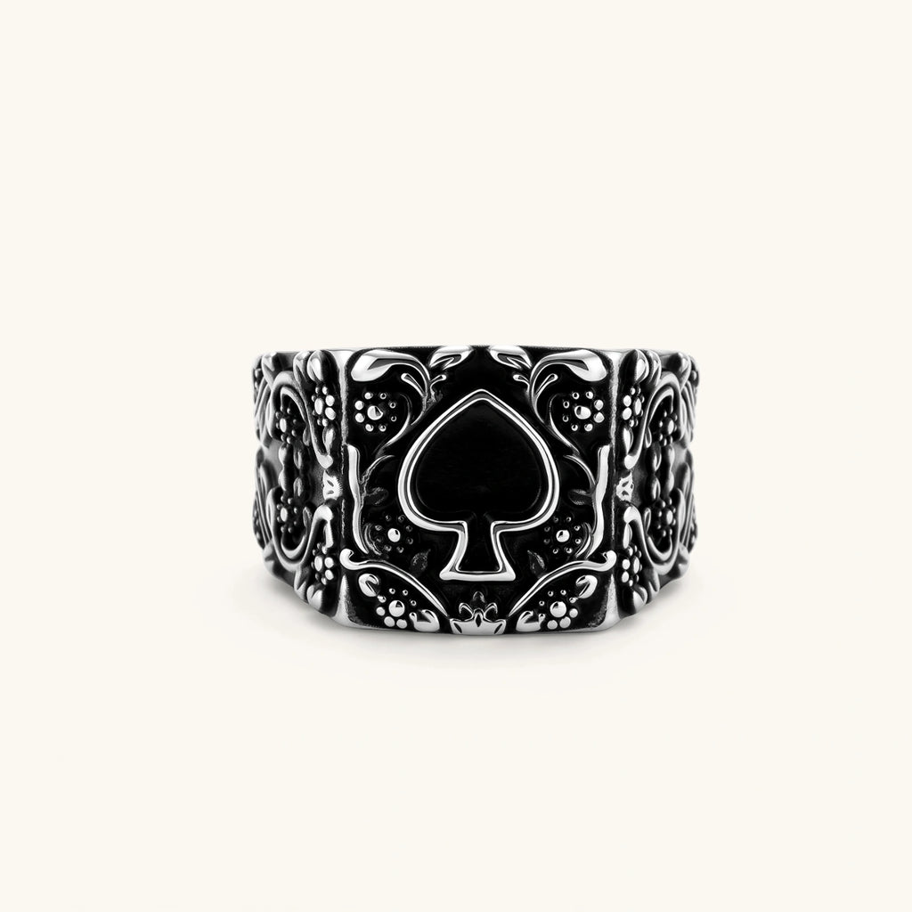 Silver-tone 316L stainless steel signet ring with black enamel spade motif and intricate floral scrollwork relief detail.