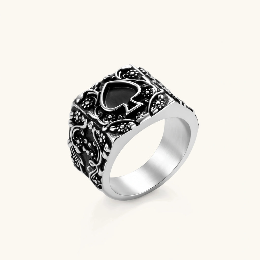 Silver-tone 316L stainless steel signet ring with black enamel spade motif and intricate floral scrollwork relief detail.
