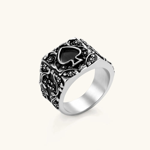 Silver-tone 316L stainless steel signet ring with black enamel spade motif and intricate floral scrollwork relief detail.
