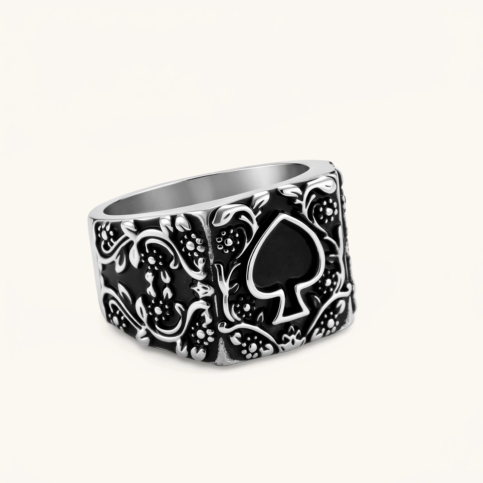 Silver-tone 316L stainless steel signet ring with black enamel spade motif and intricate floral scrollwork relief detail.