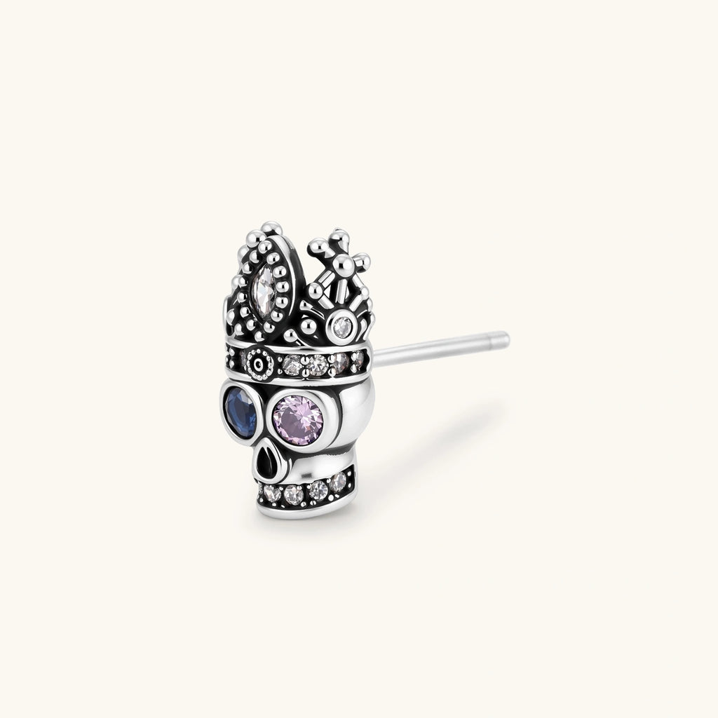 316L stainless steel skull stud earring with ornate crown top, blue and pink CZ eyes, and clear CZ accents on white background.