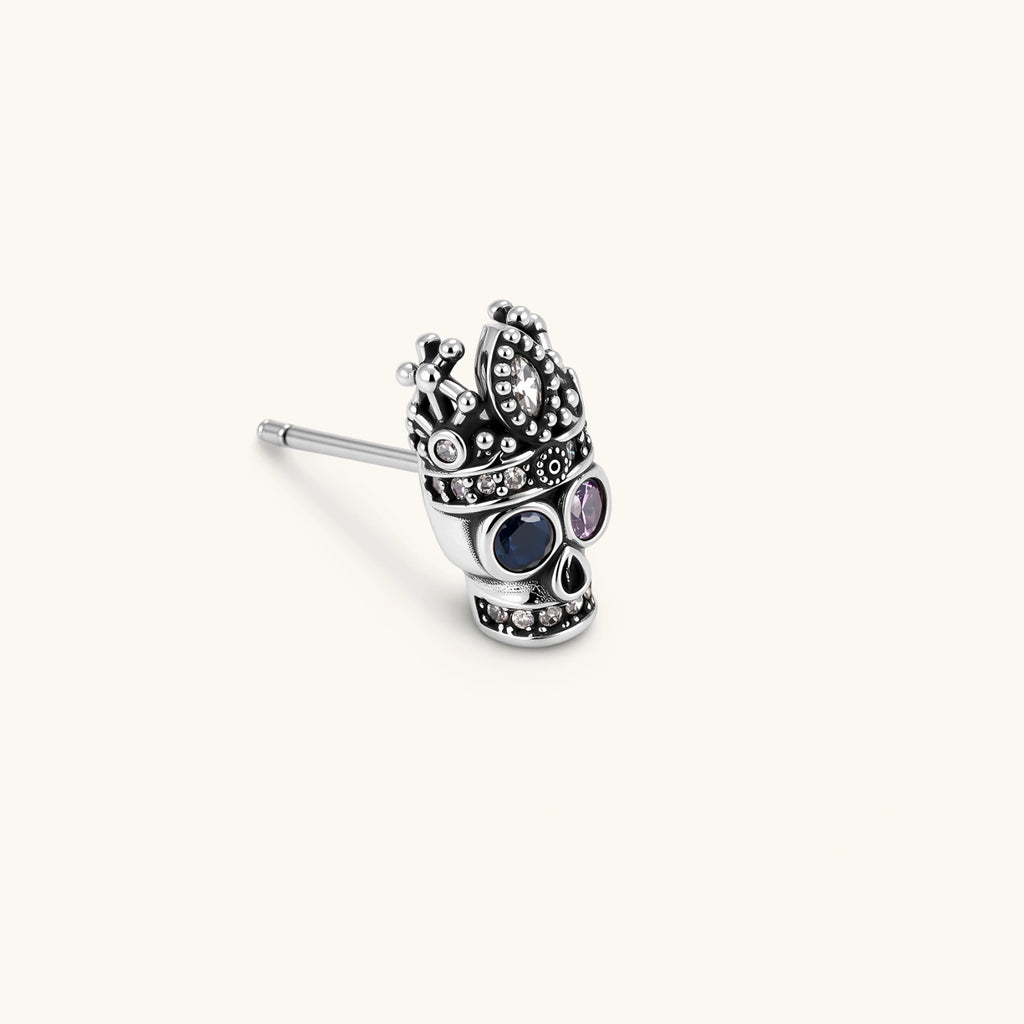 316L stainless steel skull stud earring with ornate crown top, blue and pink CZ eyes, and clear CZ accents on white background.