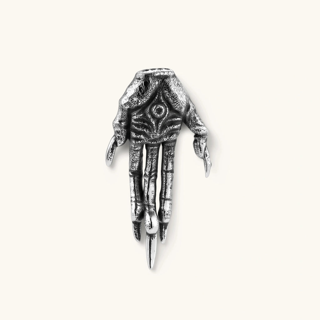 Silver stainless steel stud earring shaped like a skeletal demon claw hand with an eye motif on the palm and sharp talon fingers.