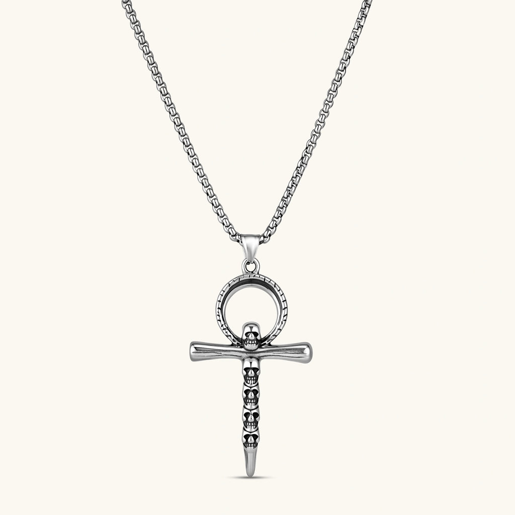 Silver stainless steel ankh pendant with skull motifs on vertical bar and textured ring top, on a box chain necklace.