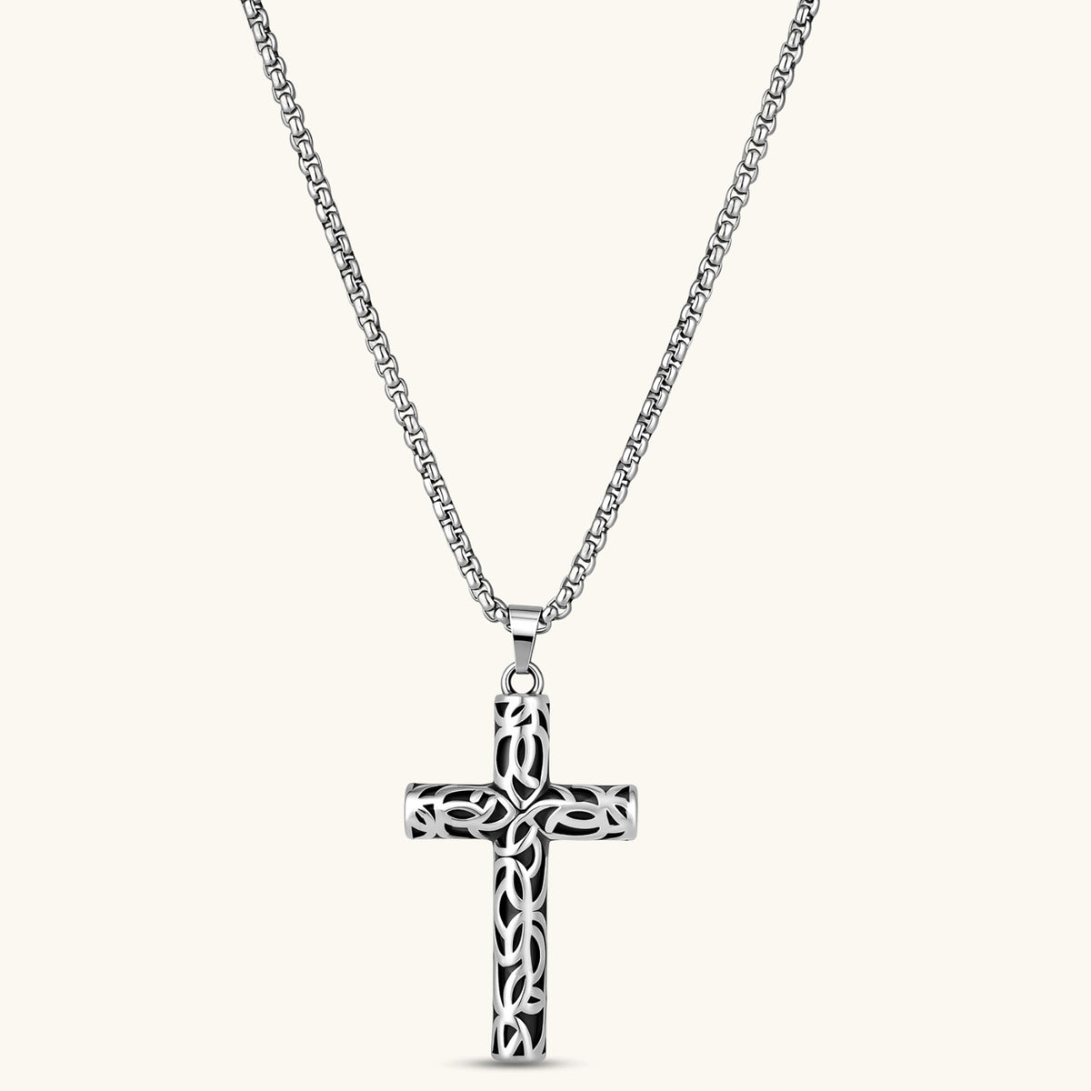 Silver stainless steel Celtic cross pendant with filigree vine pattern on a box chain, against a cream background.