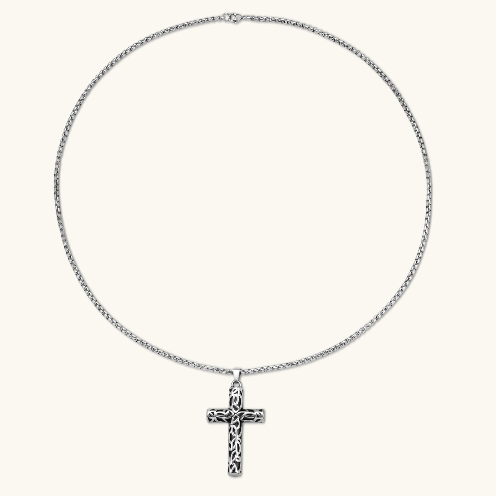 Silver stainless steel Celtic cross pendant with filigree vine pattern on a box chain, against a cream background.