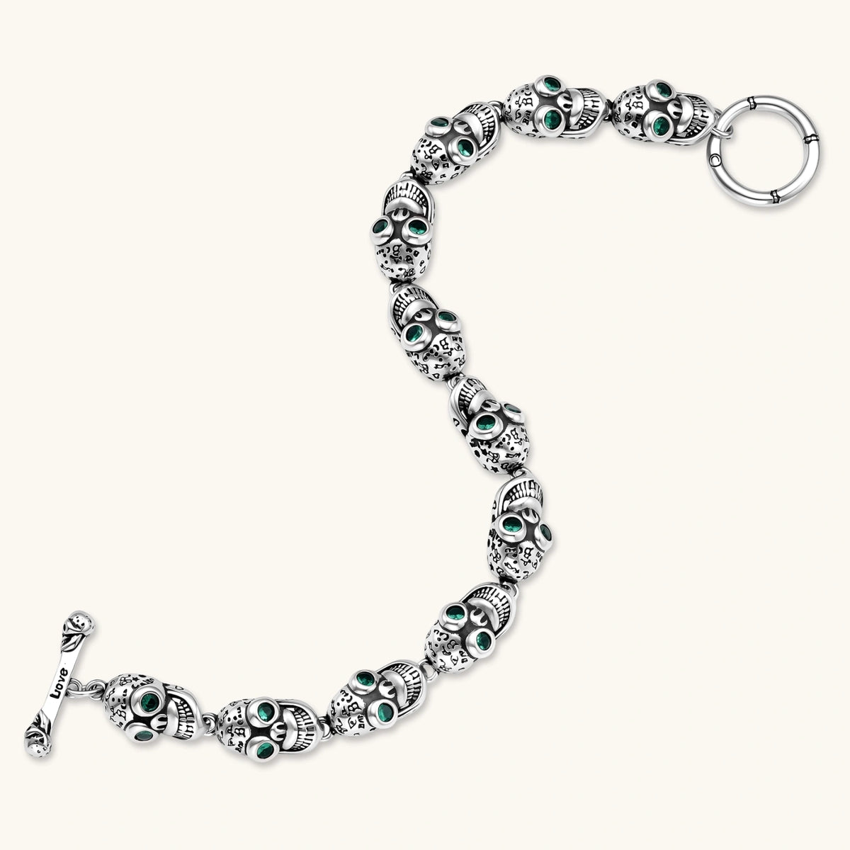 Silver stainless steel skull link bracelet with green crystal eye sockets and engraved detailing, toggle clasp closure.