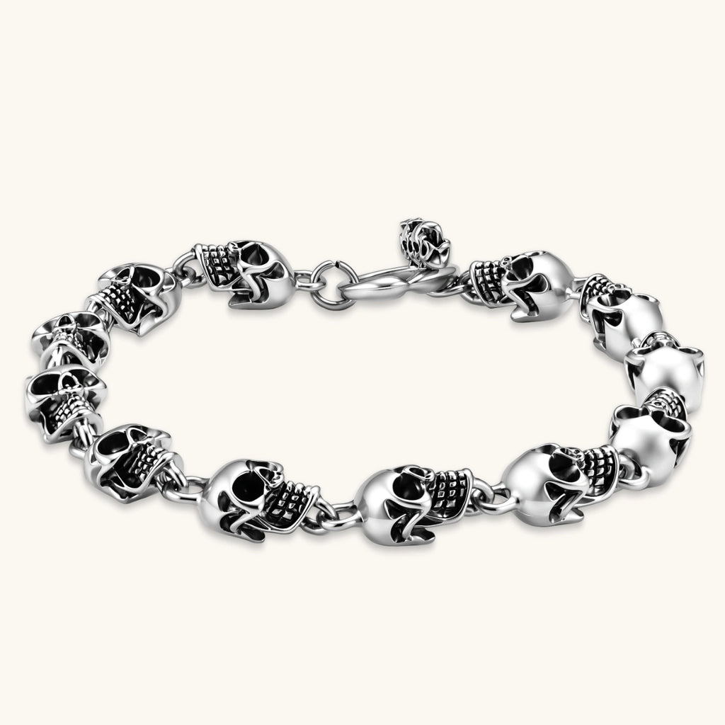 Silver stainless steel bracelet with linked 3D skull charms and a spring-ring clasp, oxidized black detailing, 225mm length.