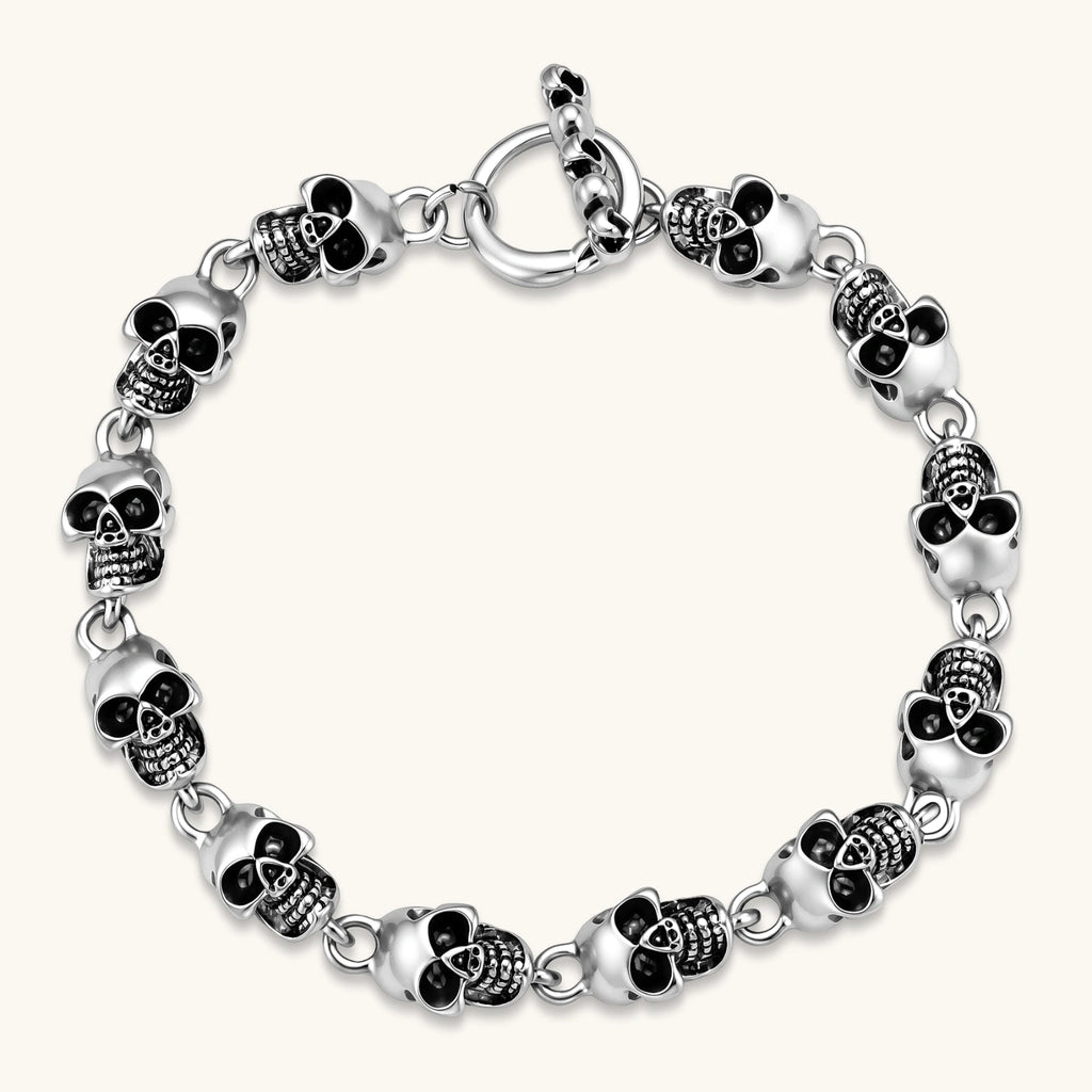 Silver stainless steel bracelet with linked 3D skull charms and a spring-ring clasp, oxidized black detailing, 225mm length.