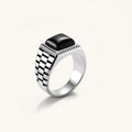 Silver stainless steel signet ring with checkered band texture, beaded border, and square black onyx cabochon stone center.